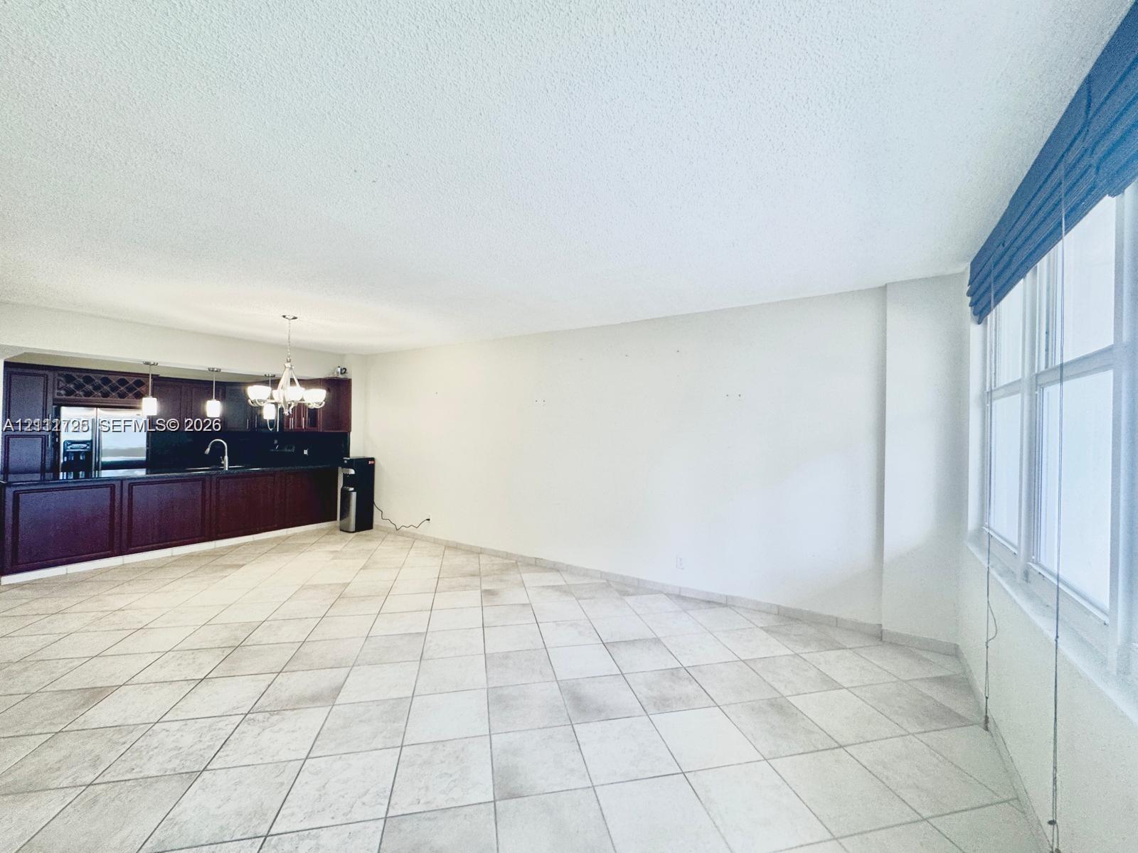 Open-concept interior featuring large-format tile flooring, recessed ceiling lighting, and a kitchen with dark wood-finish cabinetry, a built-in wine rack, and a dark countertop