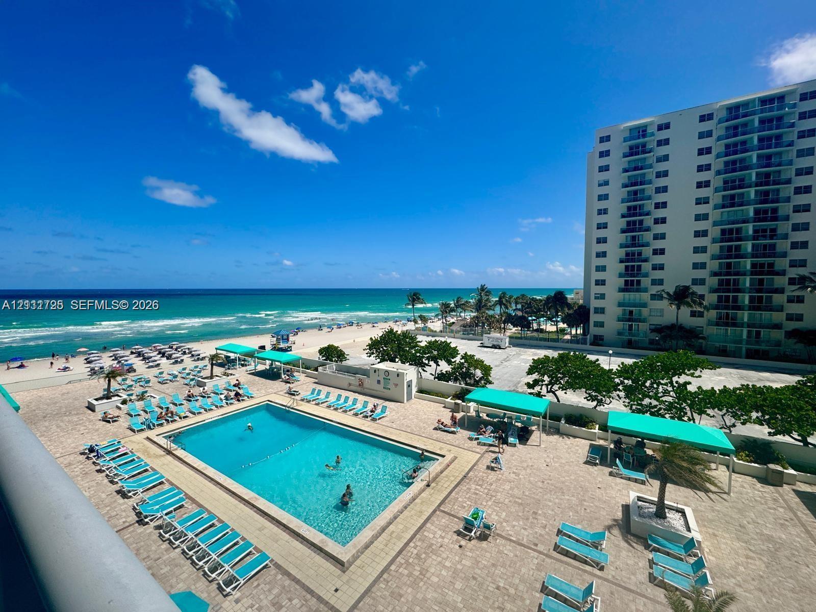 Community swimming pool with a paved deck, turquoise water, and expansive ocean scenery