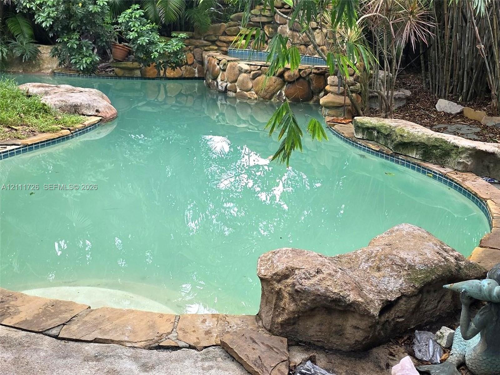 Freeform swimming pool featuring a natural stone border, integrated stone waterfall, built-in tiled spa, and large decorative boulders Freeform swimming pool featuring a natural stone border, integrated stone waterfall, built-in tiled spa, and large decorative boulders