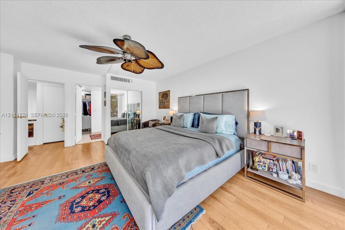 Room featuring wood-finish flooring, a ceiling fan with leaf-style blades, and a closet with mirrored sliding doors