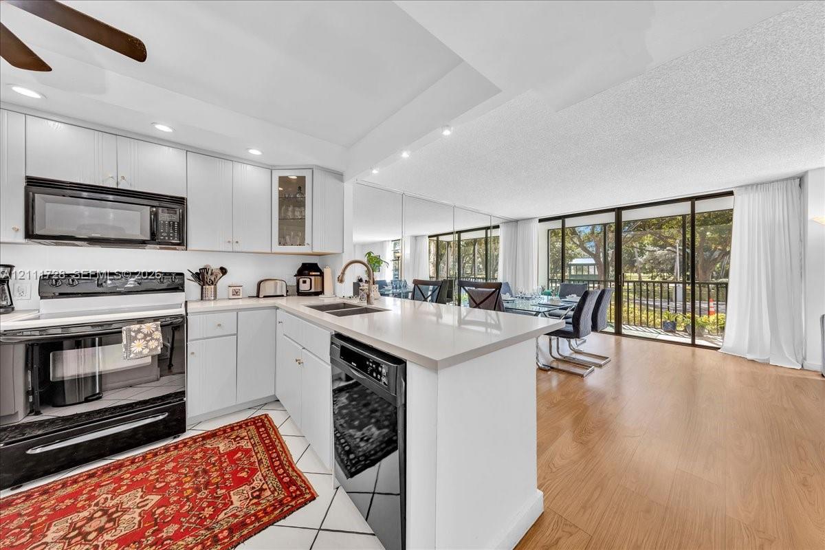 Kitchen featuring white cabinetry, solid surface countertops, a stainless steel dishwasher, wood-finish flooring, and a mirrored wall panel