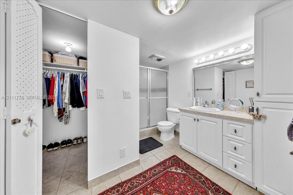 Bathroom featuring a white vanity with drawers, a light-toned solid surface countertop, an integrated sink, a full-width vanity mirror, and a walk-in shower with a glass enclosure
