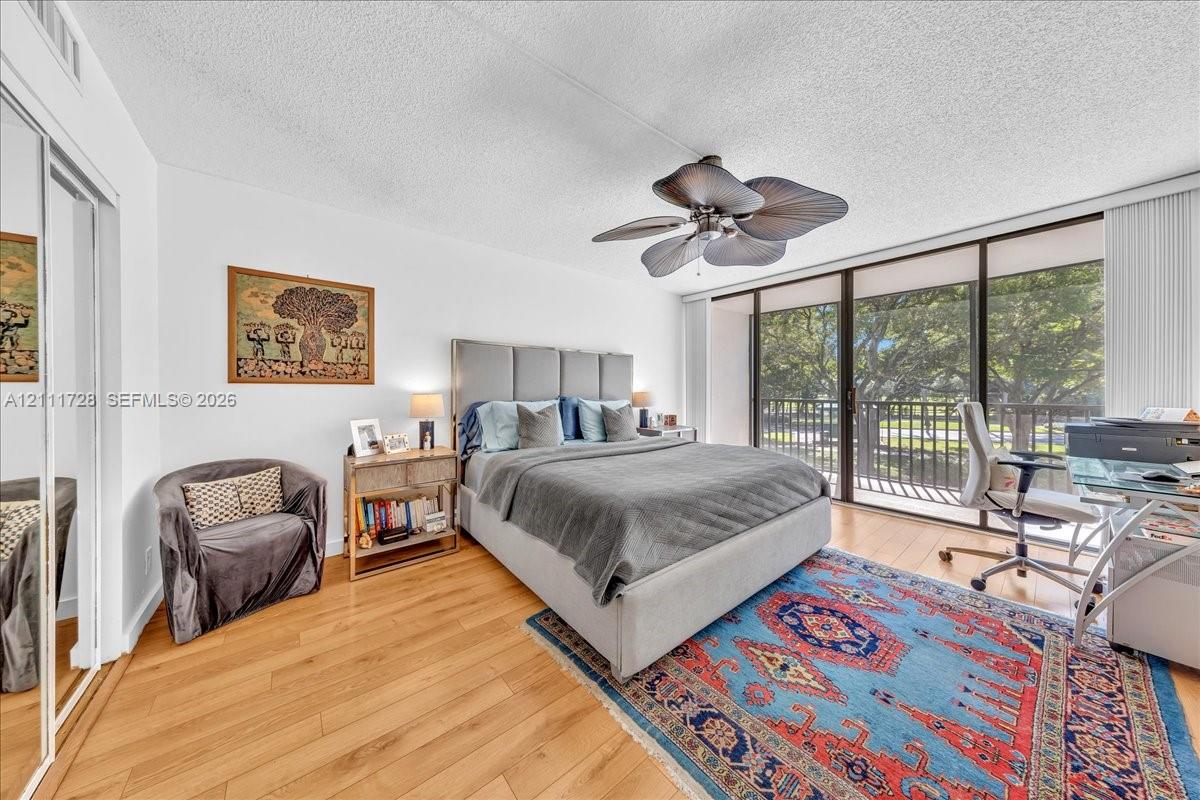 Wood-finish flooring, floor-to-ceiling glass sliding doors, private balcony, mirrored closet doors, and leaf-blade ceiling fan