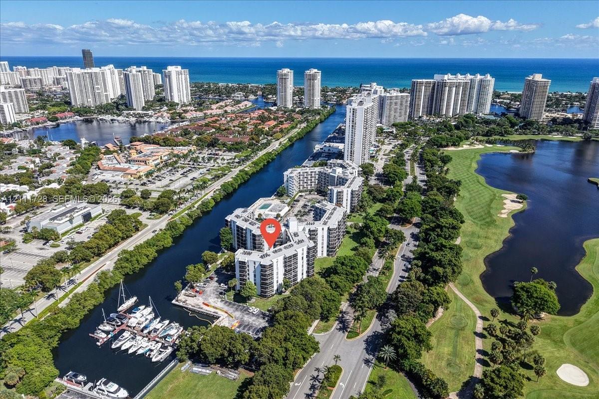 Aerial perspective of high-rise multi-family residential building situated between a waterway with deep-water boat slips, a sprawling golf course, and the Atlantic coastline