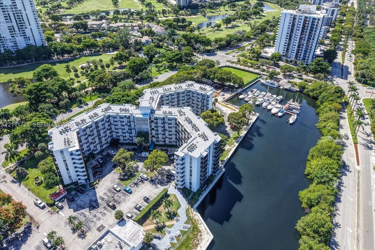Aerial perspective of waterfront mid-rise building featuring private boat slips, paved surface parking, and mature landscaping