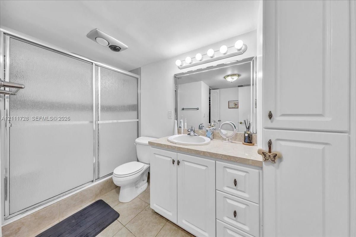 Bathroom featuring a vanity with white cabinetry and a solid-surface countertop, an integrated sink with a chrome faucet, a shower enclosure with frosted sliding doors, and built-in floor-to-ceiling storage cabinetry