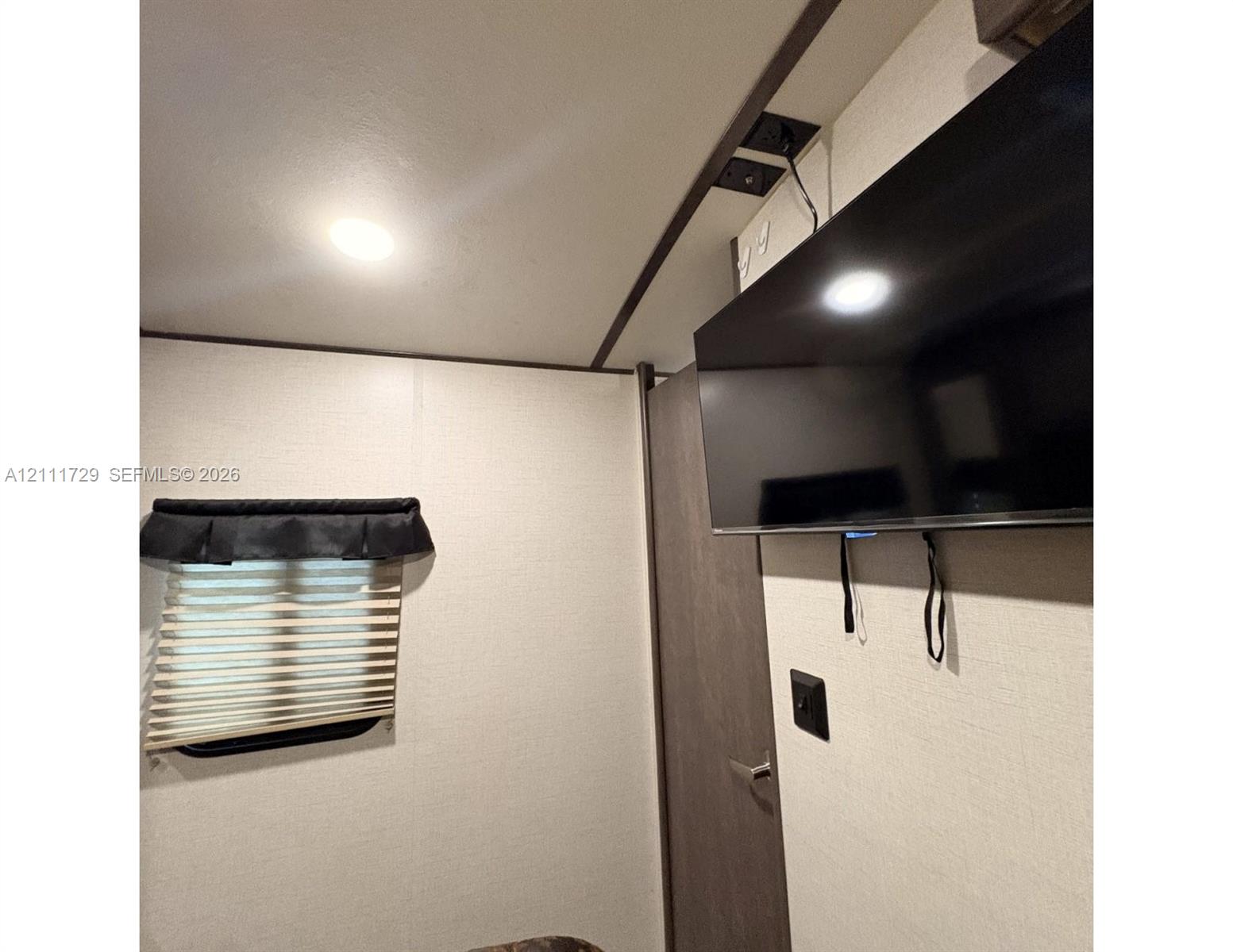Wall-mounted flat screen television with integrated power and media connections, recessed ceiling lighting, and a pleated accordion window shade