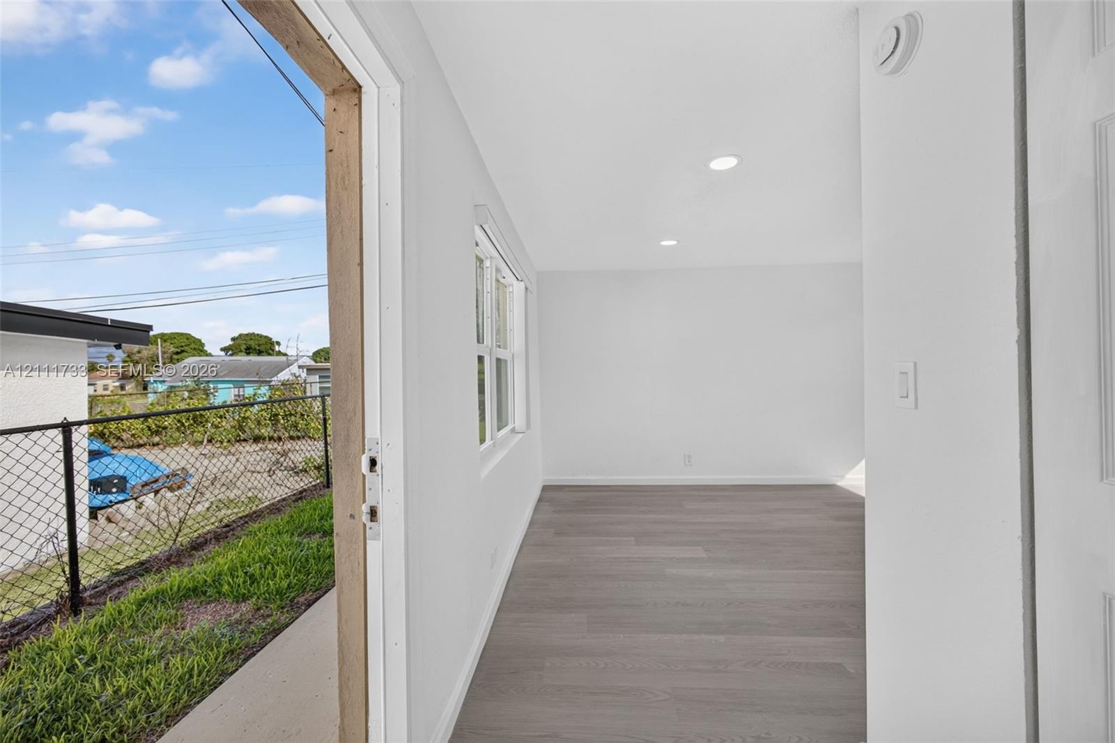 Interior view from front area thru door (lock-off) to rear bedroom and showing open rear exterior entry door to left. featuring wood-finish flooring, recessed lighting, and a multi-pane window