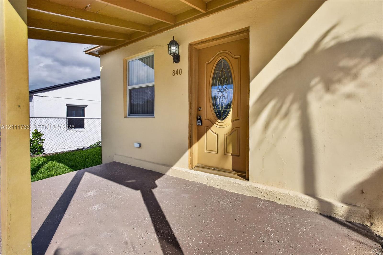 Covered front porch featuring a solid front door with an oval glass insert, exterior wall-mounted light fixture, and horizontal window