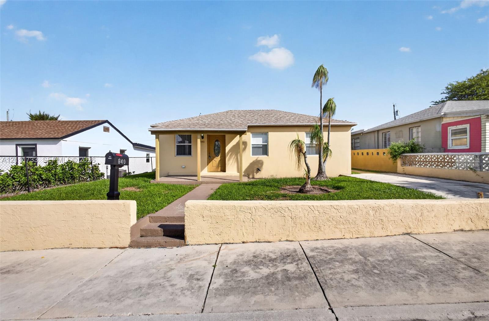 Single-story exterior featuring a stucco facade, covered front porch, concrete driveway, and a low-profile masonry perimeter wall