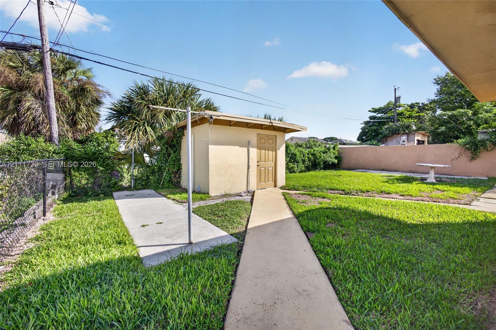 Rear yard from left side of home, featuring a detached shed with laundry room, concrete pathways, perimeter masonry wall.