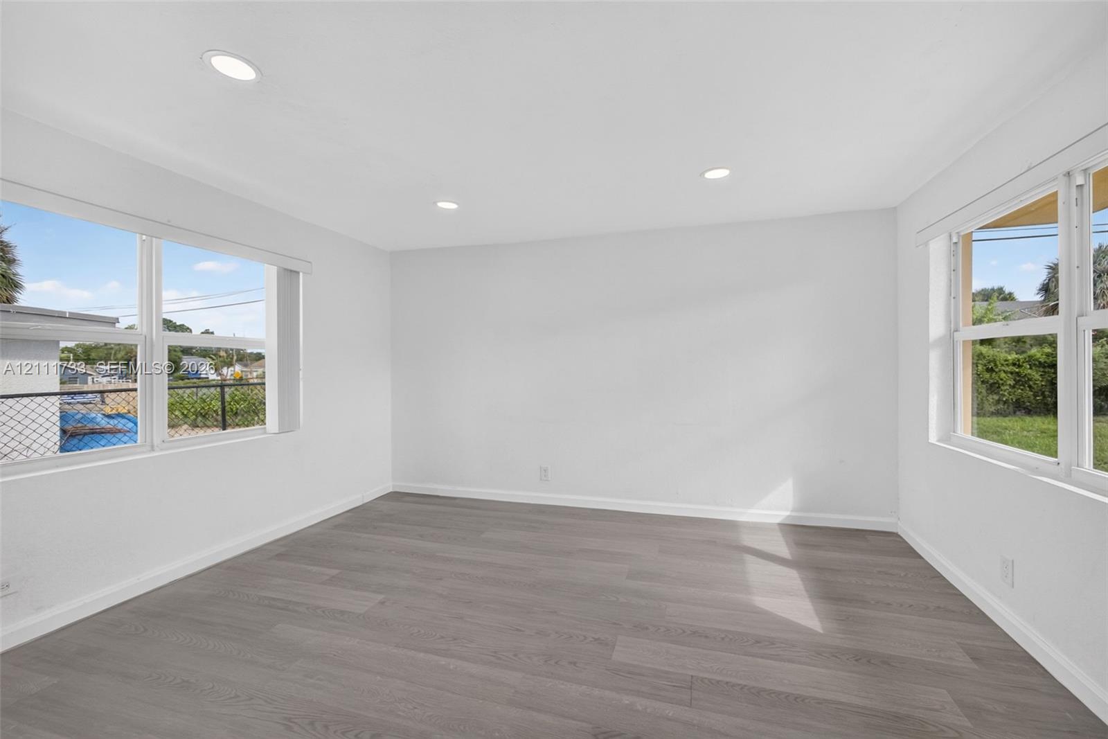 Rear bedroom features Neutral-toned wood-finish flooring, recessed lighting, and multiple large windows with white trim