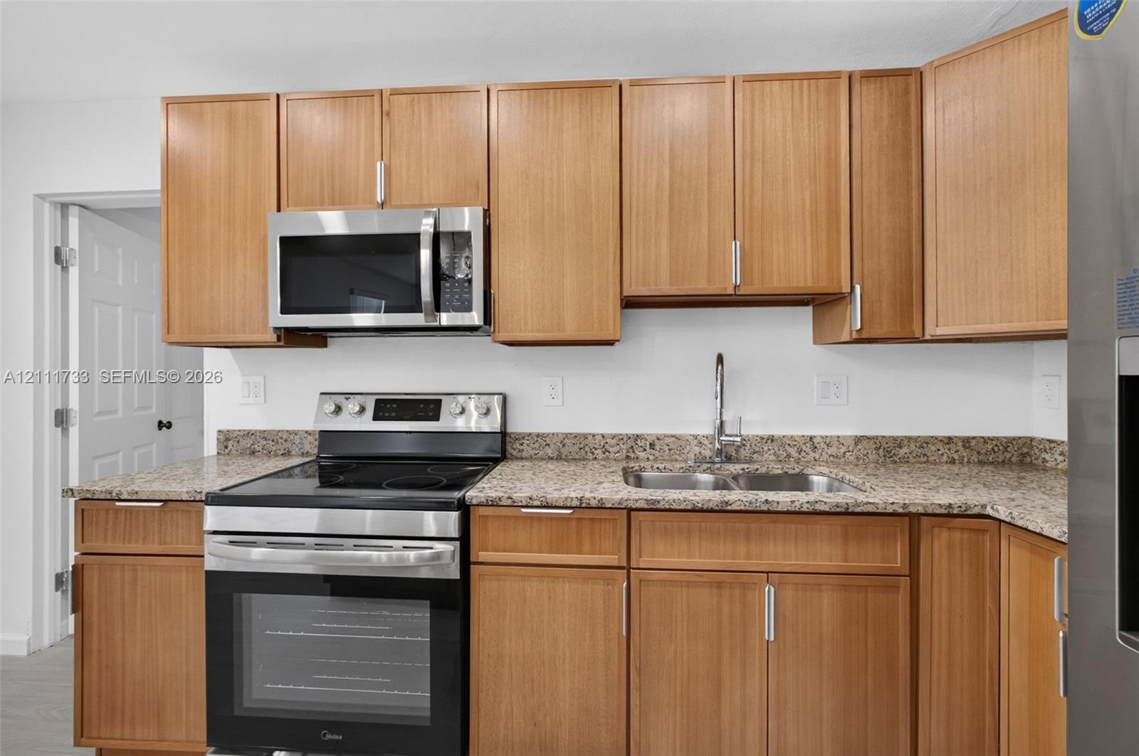 Kitchen featuring wood-finish cabinetry, stone-patterned countertops, a stainless steel electric range, an over-the-range microwave, and a dual-basin sink with a chrome faucet