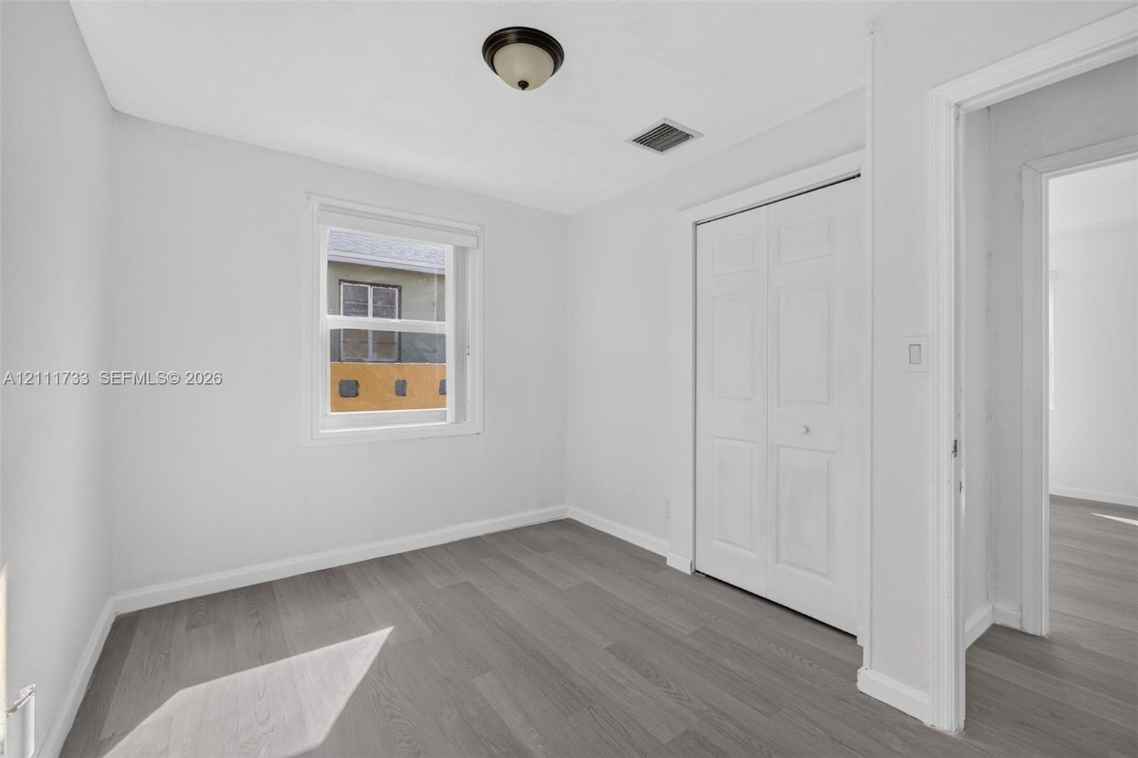 Neutral-toned room featuring grey wood-finish flooring, double-panel closet doors, and a single-hung window with a white frame