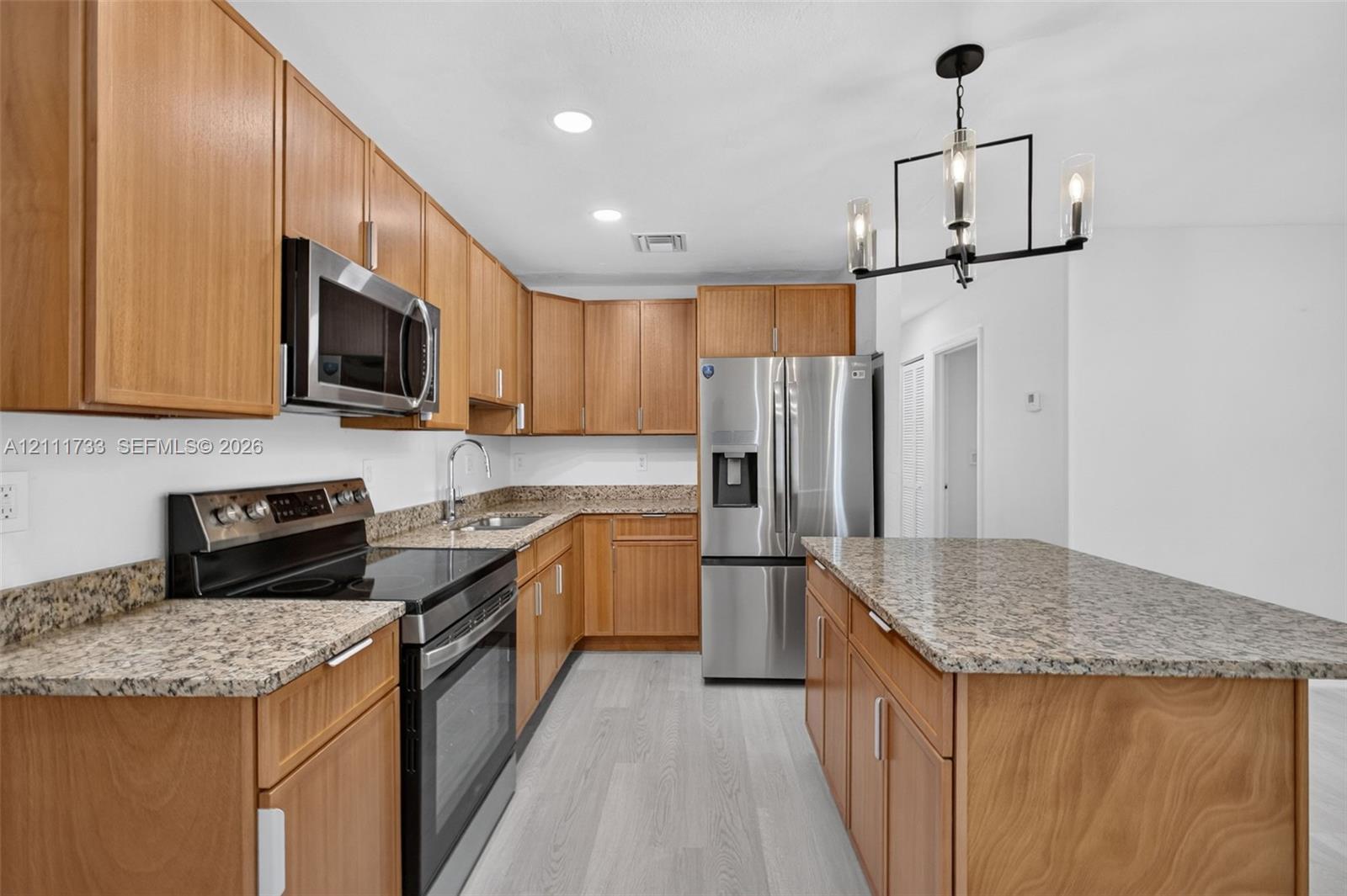 Kitchen featuring natural wood cabinetry, stone-surface countertops, a center island, stainless steel appliances, and recessed lighting