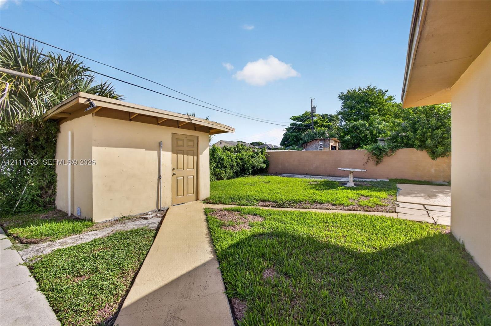 Backyard featuring a concrete walkway, detached Shed with Laundry Room, grass lawn, and concrete walk way.