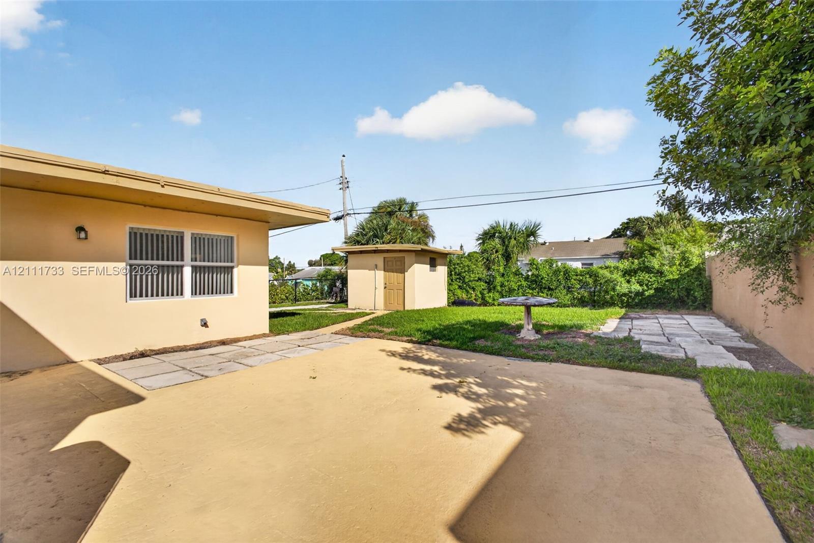 Rear exterior space featuring a concrete patio, a detached shed with laundry room, stone paver accents, and a grass lawn area.