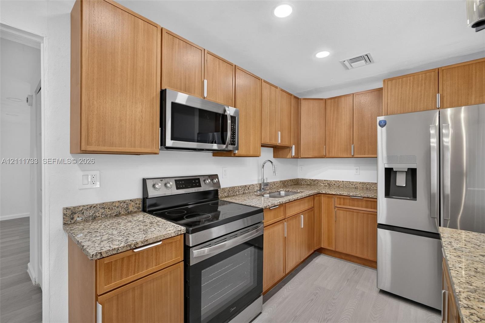 Kitchen featuring wood cabinetry, stone-finish countertops, stainless steel appliances, and wood-finish flooring
