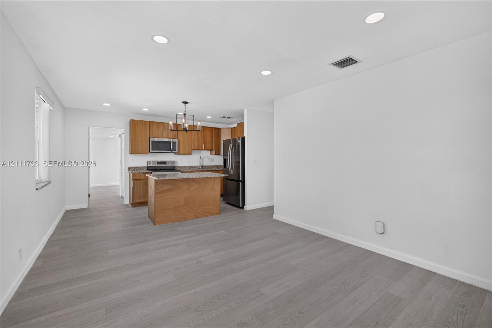 Kitchen featuring wood-finish cabinetry, an island, stone-surface countertops, stainless steel appliances, and recessed ceiling lighting throughout