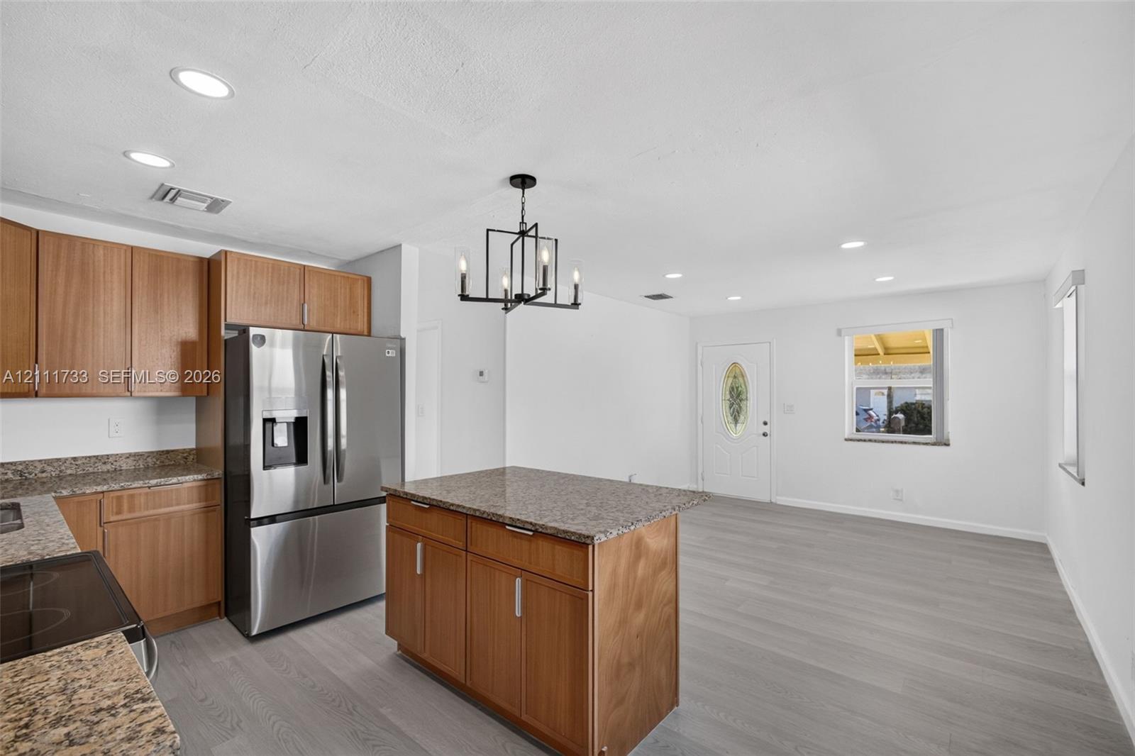 Kitchen featuring medium-tone wood cabinetry, stone countertops, central island, stainless steel refrigerator, and recessed lighting