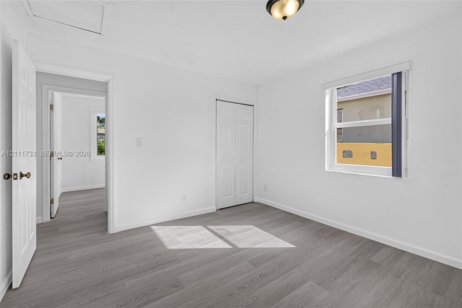 Room featuring wood-finish flooring, a single-panel interior door, a two-panel closet door, and a single-hung window with a flush-mount light fixture