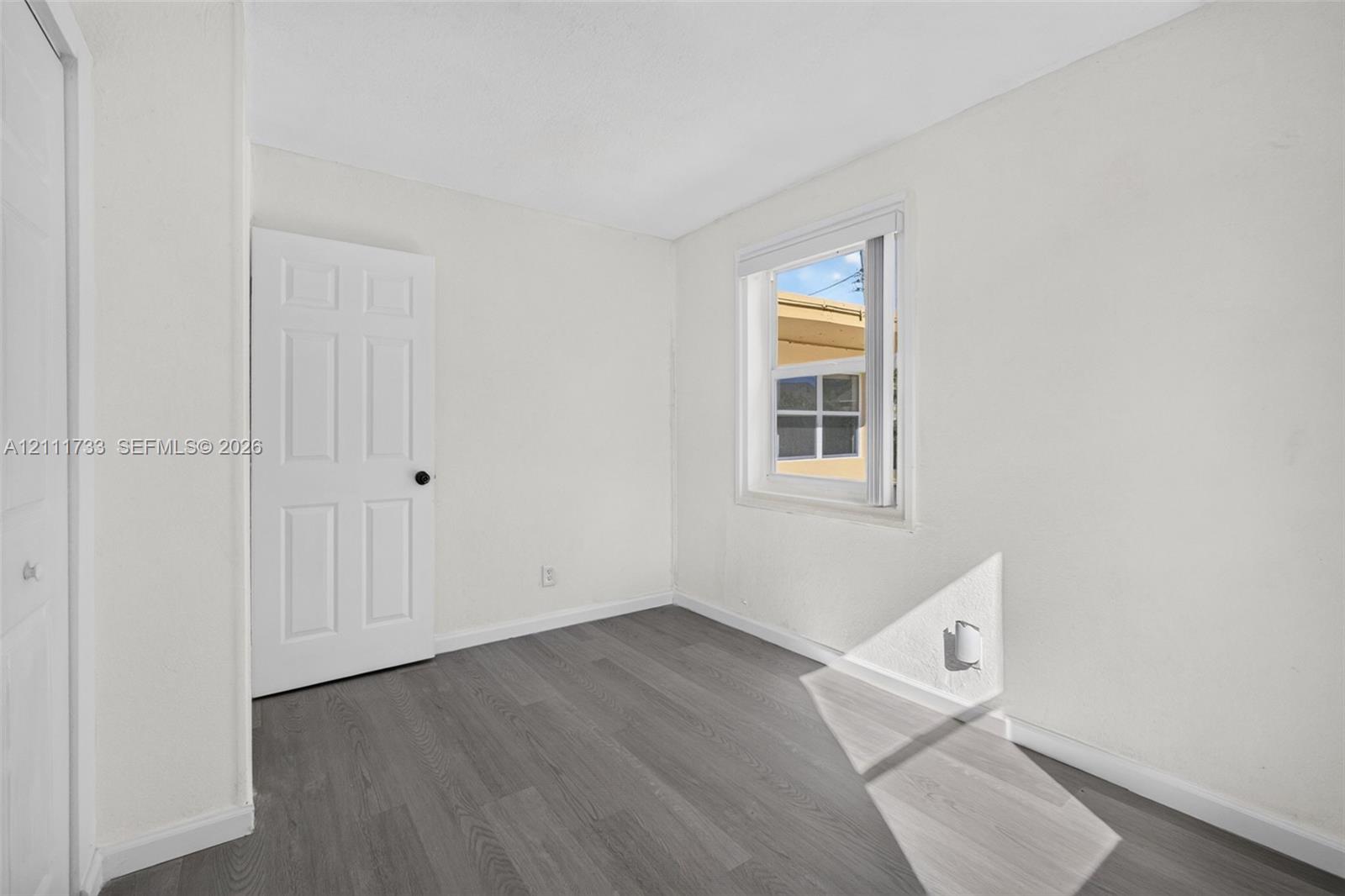 Front bedroom viewfeaturing wood-finish flooring, a single-panel interior door, and a white-framed window