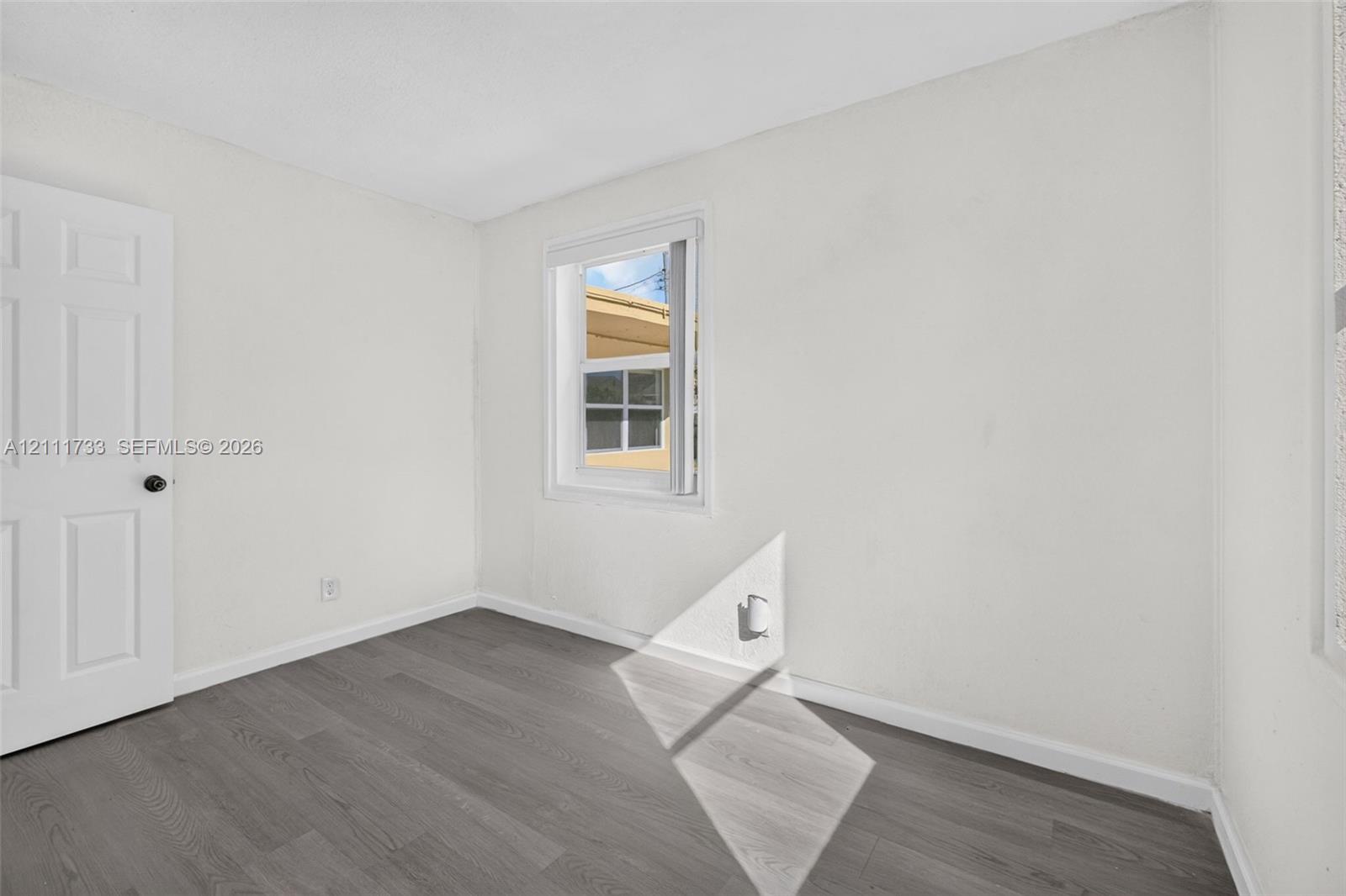 Neutral-toned wood-finish flooring, single-panel interior door, and a white-framed window