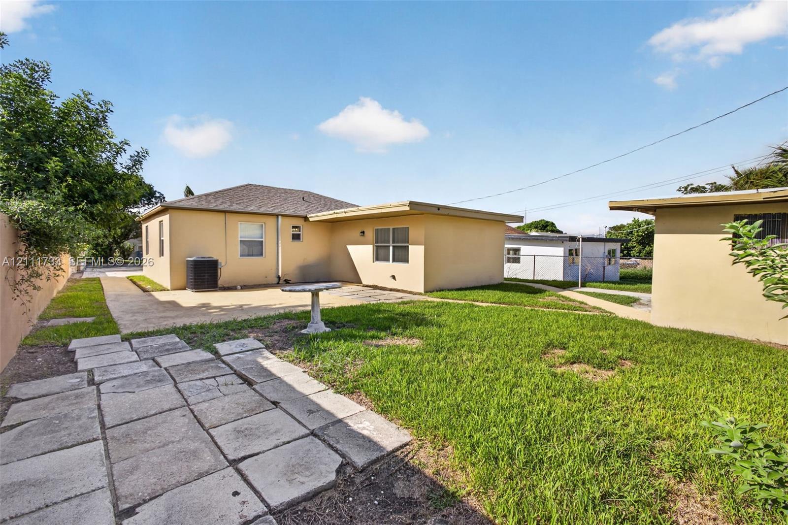 Backyard featuring a concrete patio, stone paver pathway, grass lawn, and stucco exterior walls