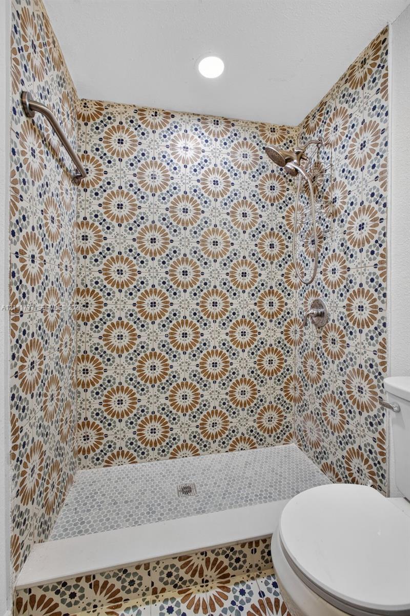 Shower stall featuring decorative patterned wall tile, a small-format mosaic tile floor, metallic finish adjustable shower head, and a horizontal metallic grab bar