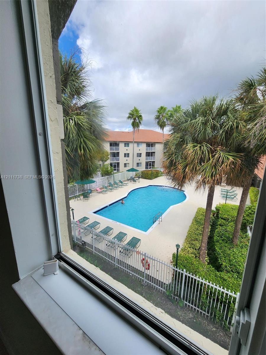 Community swimming pool featuring a concrete deck, metal perimeter fencing, and surrounding palm trees Community swimming pool featuring a concrete deck, metal perimeter fencing, and surrounding palm trees