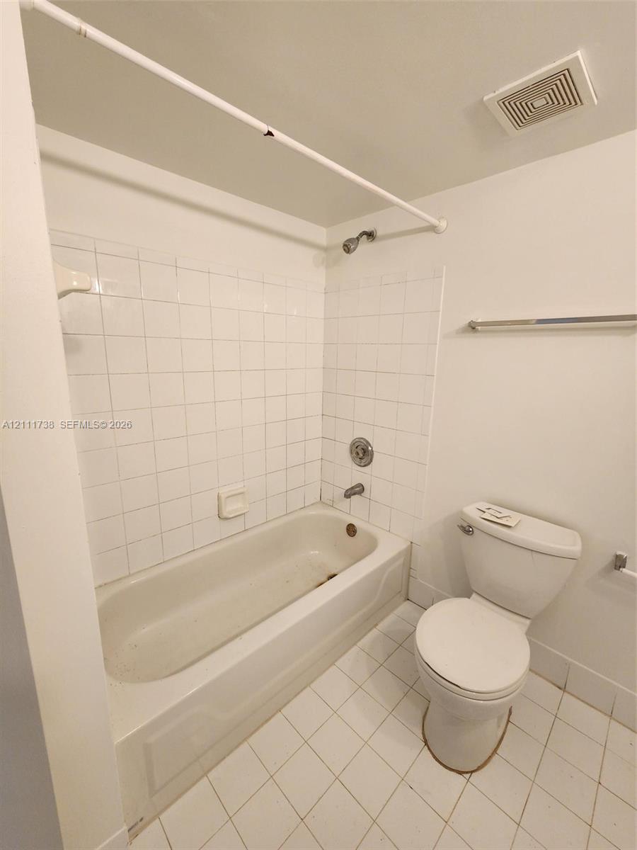 Bathroom featuring a white porcelain tub, square wall tiling, ceramic tile flooring, and a standard-height toilet Bathroom featuring a white porcelain tub, square wall tiling, ceramic tile flooring, and a standard-height toilet