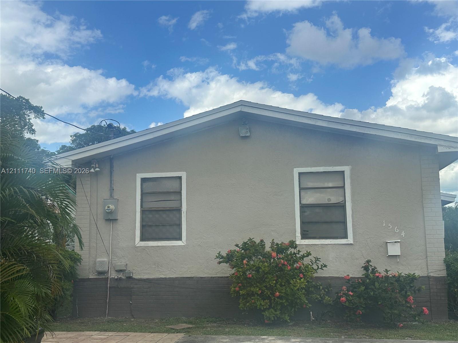 Stucco exterior featuring two single-hung windows, a gable roofline, and established landscaping