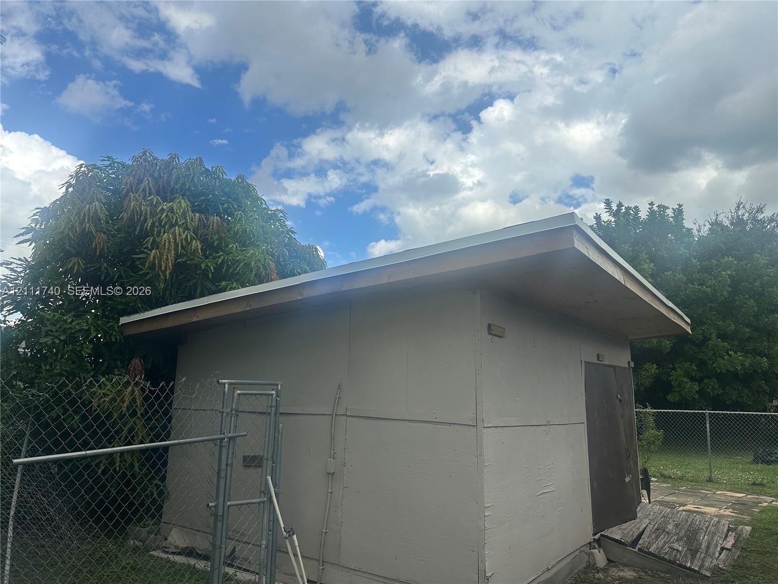 Detached exterior structure featuring a shed roof, solid-panel door, and chain-link fencing