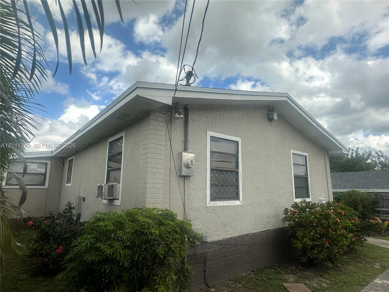 Stucco exterior featuring brick skirting, dual-pane windows, and a gable roofline