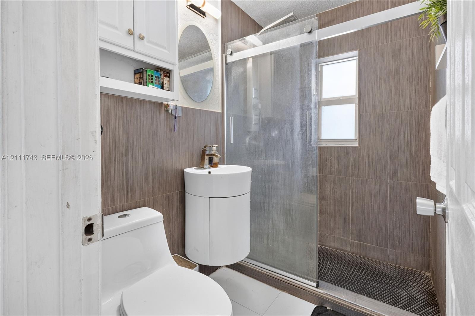 Bathroom featuring wall-to-wall vertical tile, sliding glass shower door, corner-mounted vanity with integrated sink, and white wall-mounted cabinetry