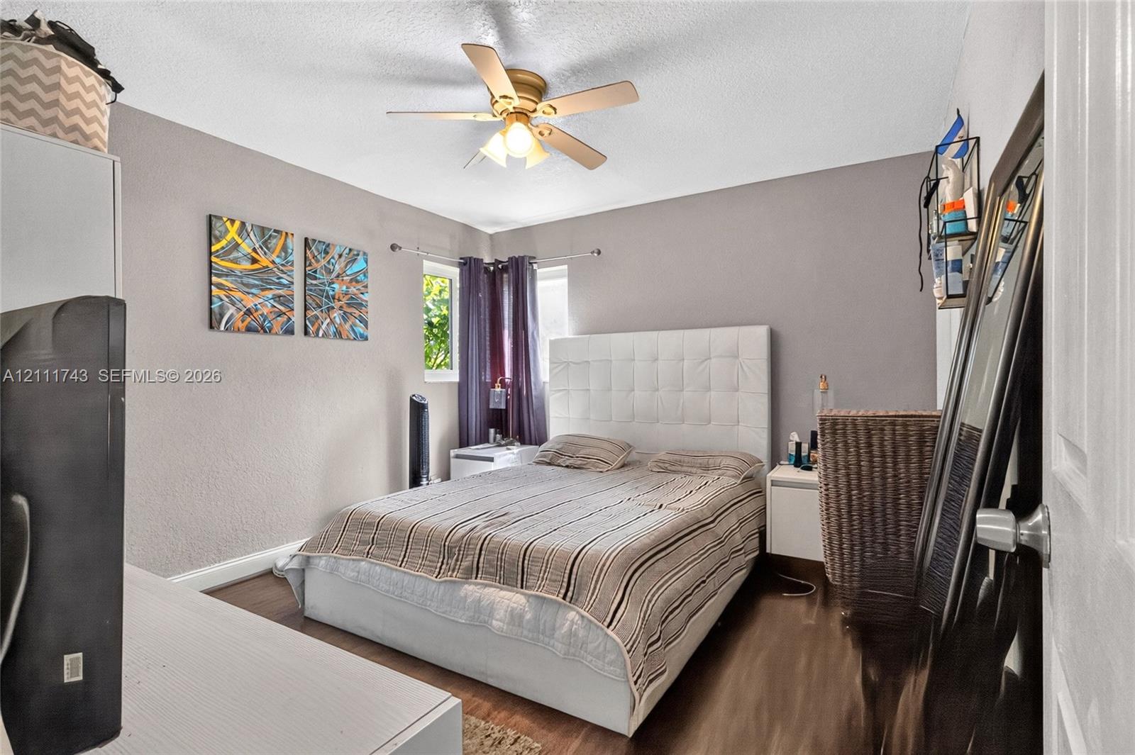 Neutral-toned interior featuring wood-finish flooring, a multi-blade ceiling fan, and corner windows