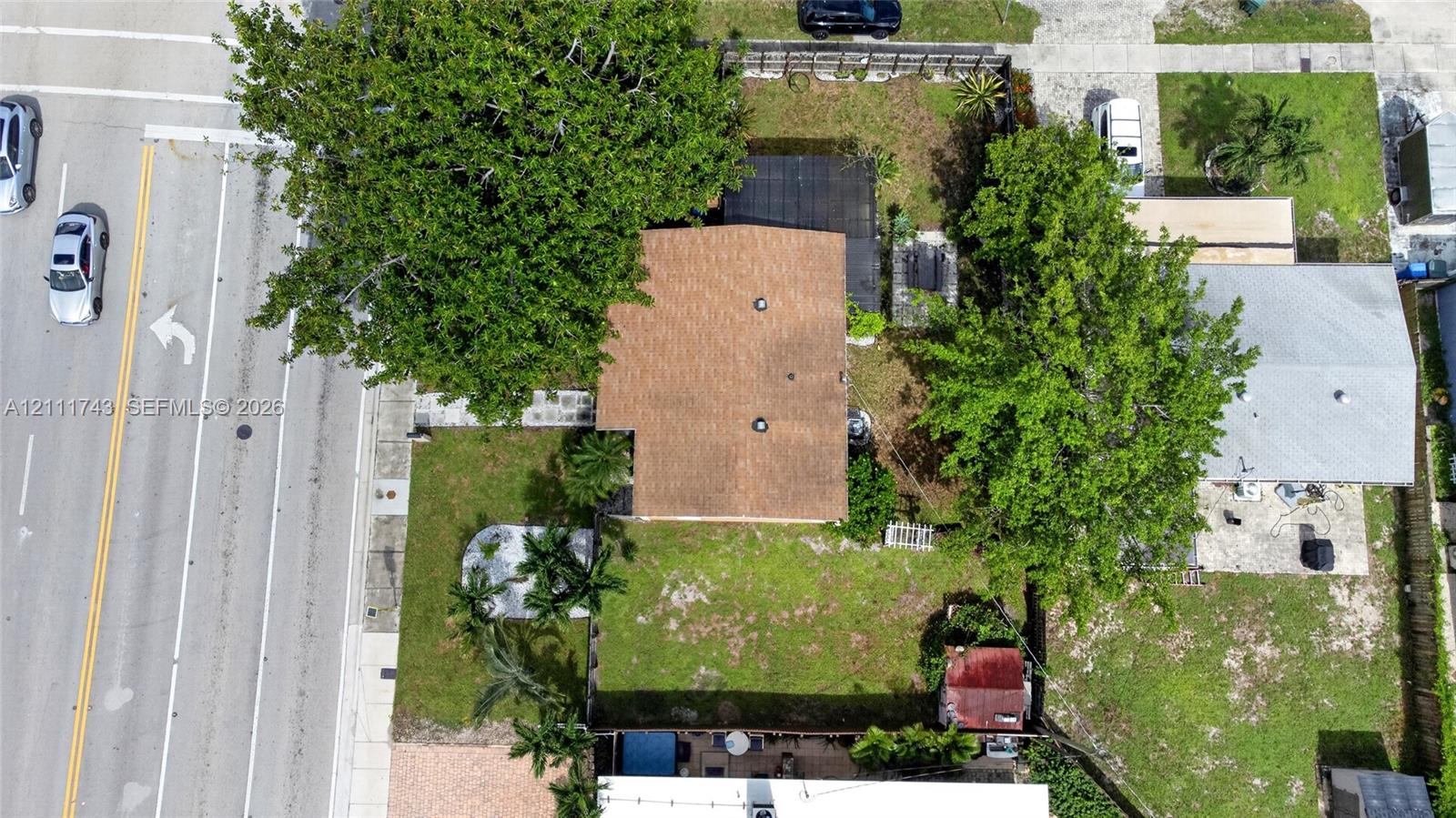 Aerial perspective featuring a residential lot with mature trees, a shingle-style roof, and a fenced backyard