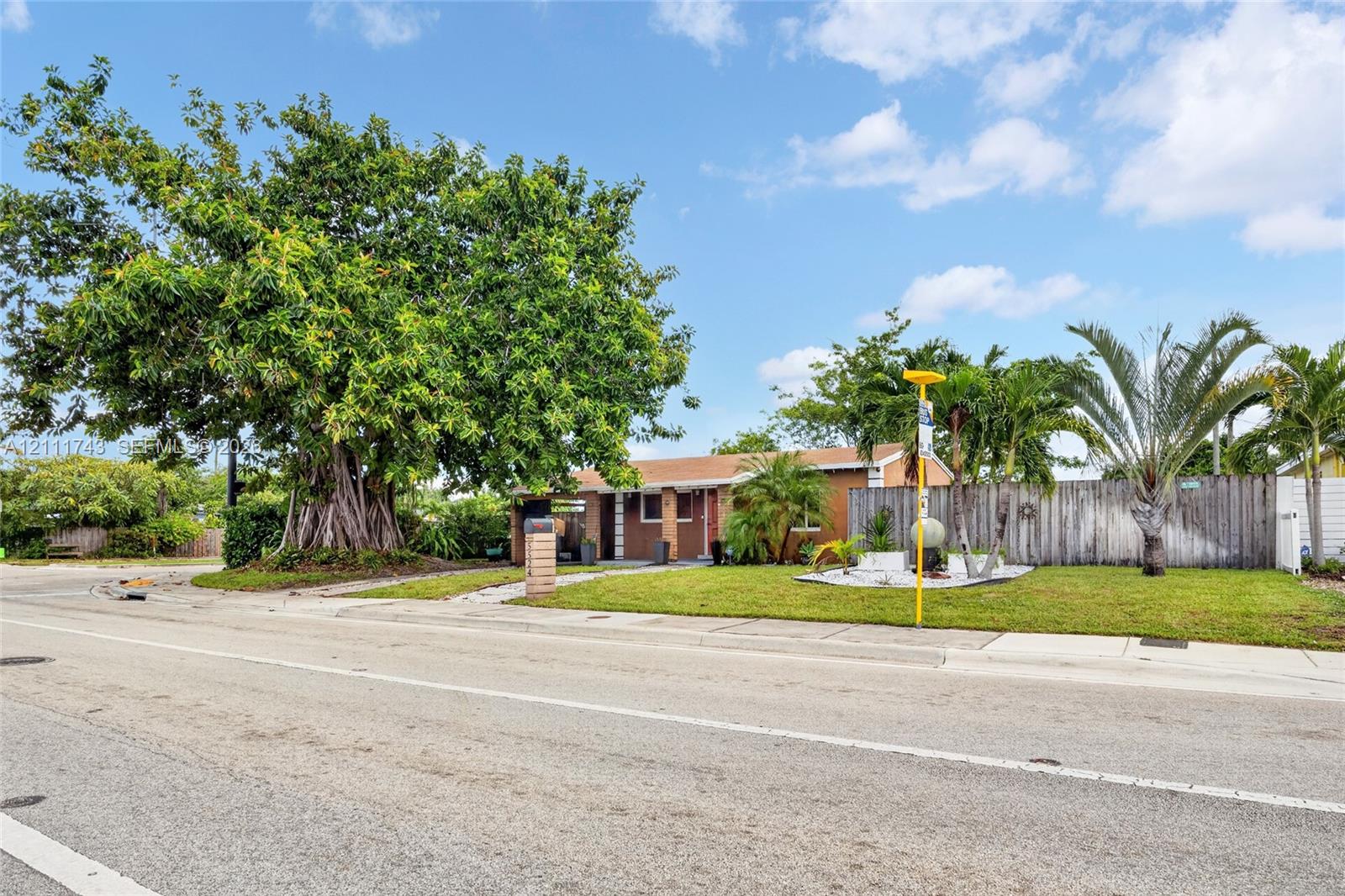 Single-story residence featuring a low-pitch roof, masonry exterior, established trees, and perimeter wood fencing