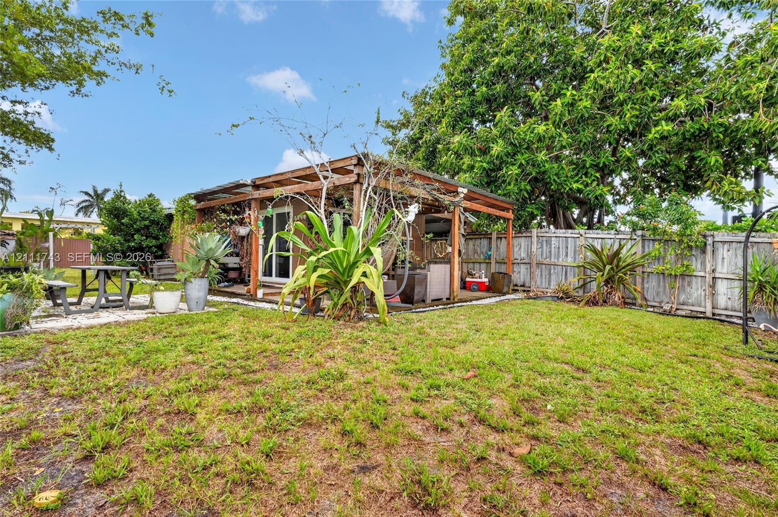Rear exterior featuring a wood-frame pergola, concrete paver accents, and wood-panel privacy fencing