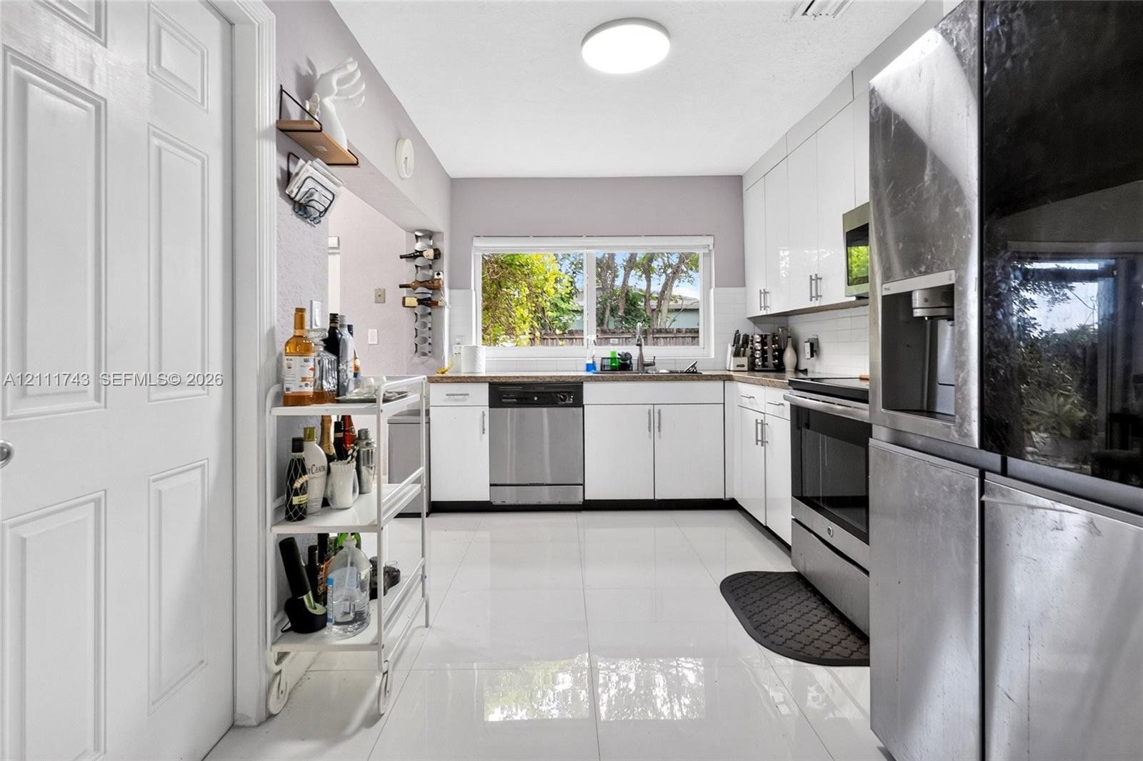 Kitchen featuring white cabinetry, stainless steel appliances, polished tile flooring, and a window above the sink