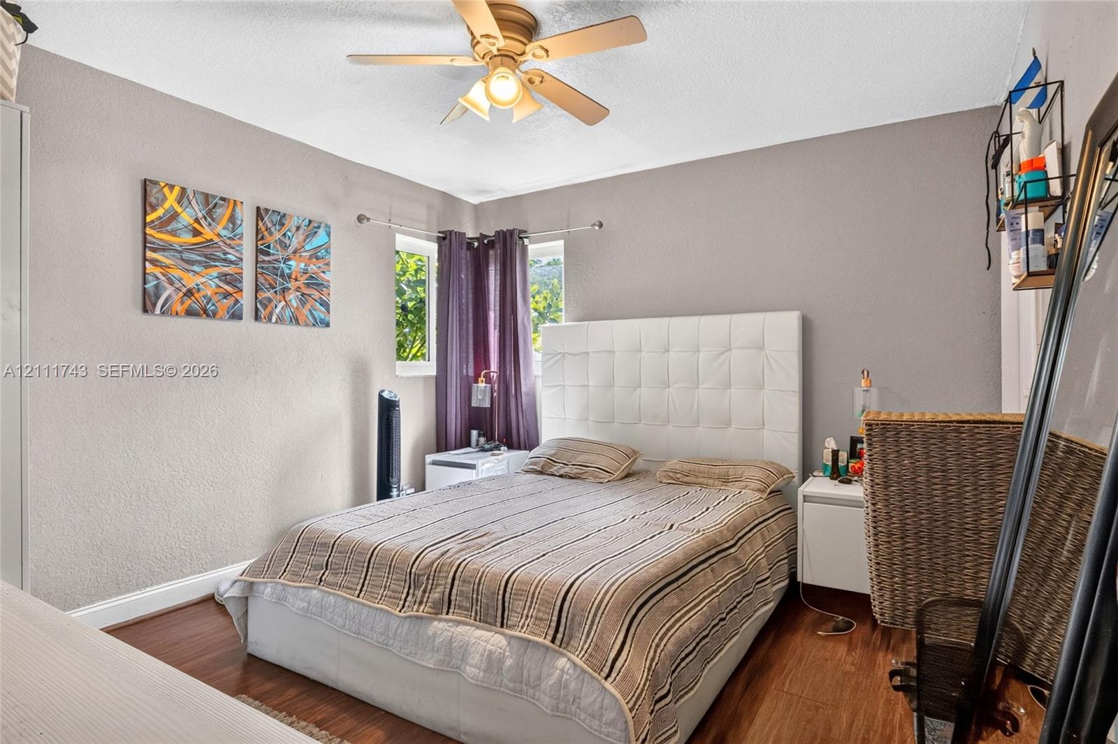 Bedroom featuring wood-finish flooring, a ceiling fan with integrated lighting, dual corner windows, and textured wall finish