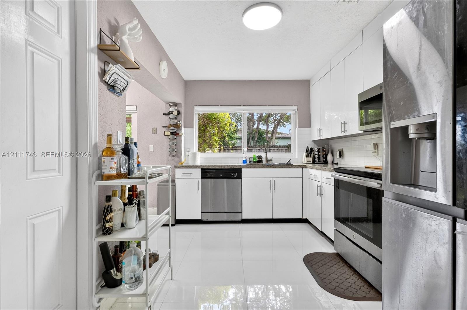 Kitchen featuring high-gloss white cabinetry, stainless steel appliances, white tile flooring, white subway tile backsplash, and a large horizontal window