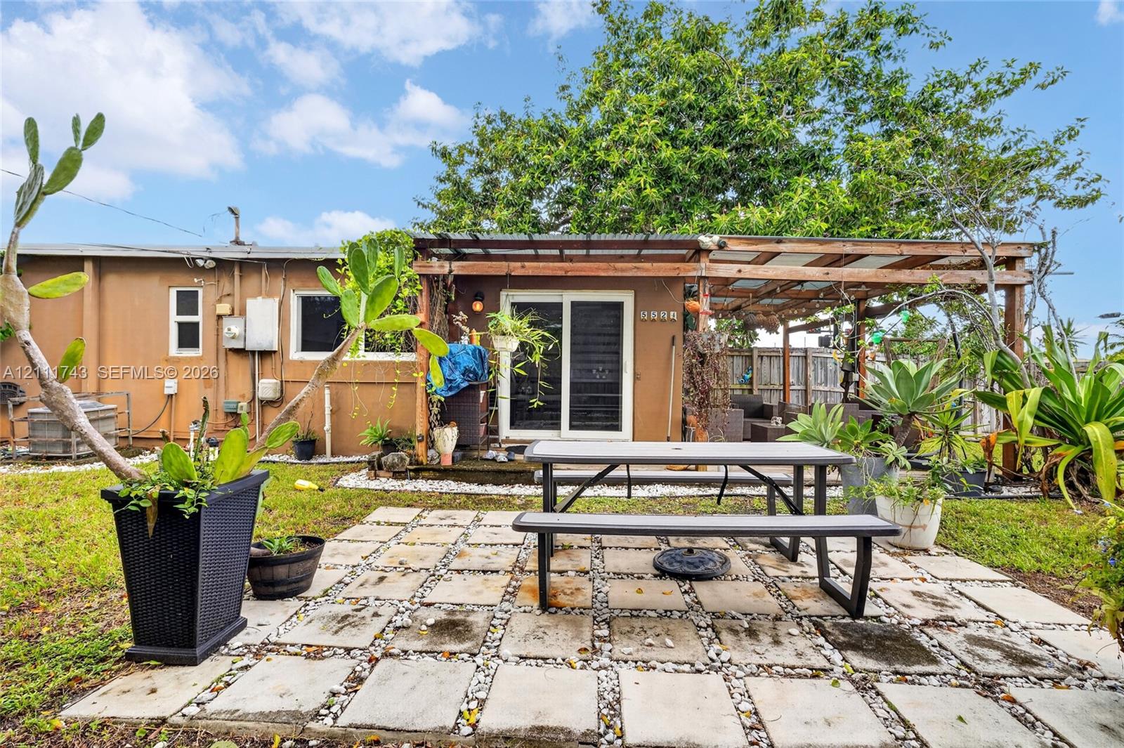 Rear exterior space featuring a square-paver patio, a wooden pergola structure, sliding glass doors, and mature landscaping