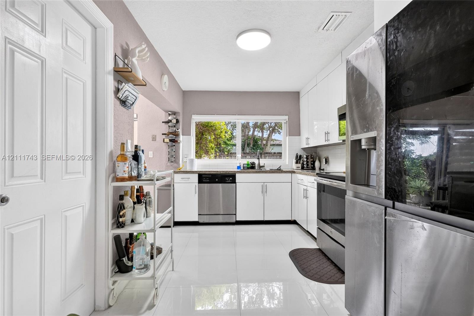 Kitchen featuring white flat-panel cabinetry, stainless steel appliances, polished tile flooring, and a window over the sink