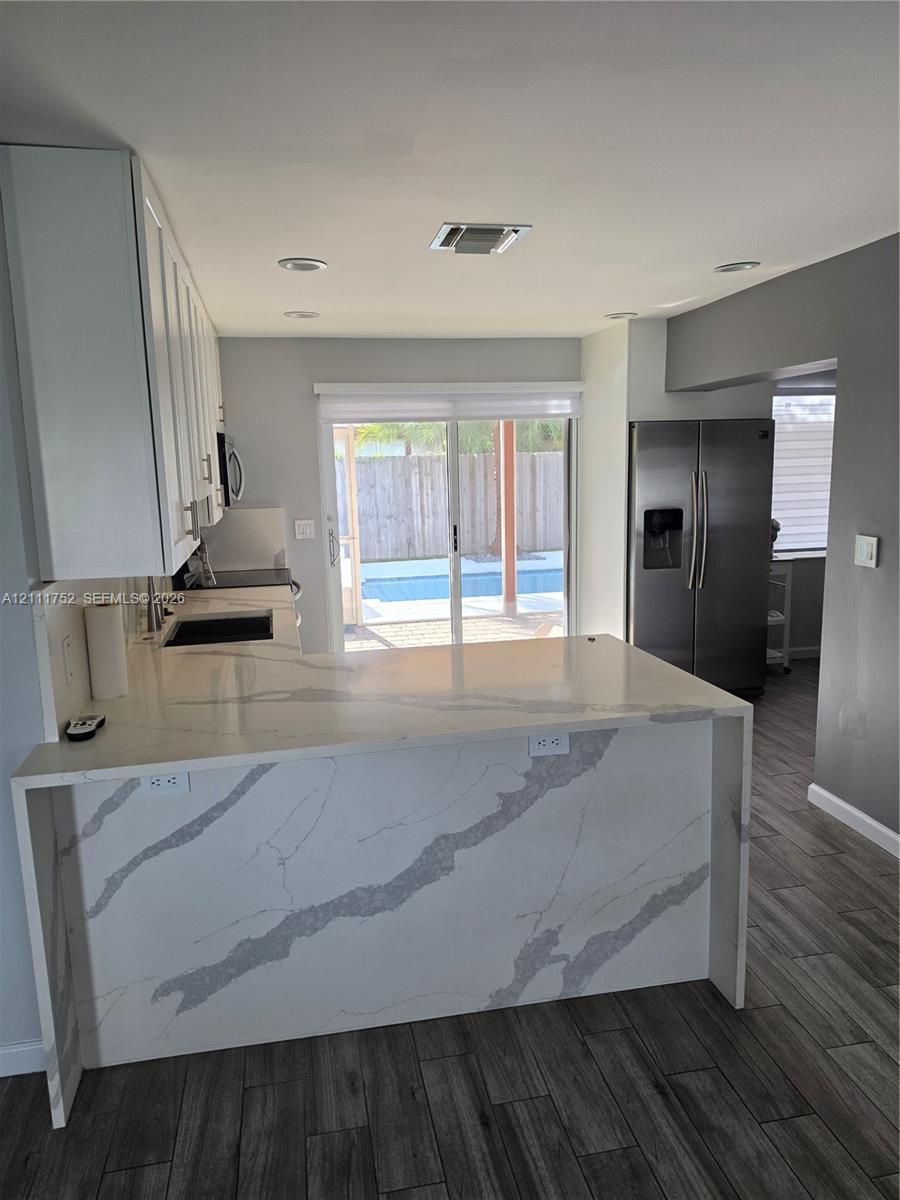 Kitchen featuring a waterfall-edge stone countertop, white shaker-style cabinetry, stainless steel refrigerator, recessed lighting, and wood-finish flooring