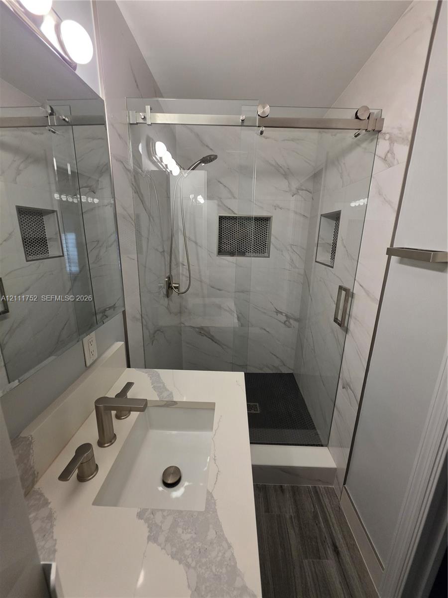 Bathroom featuring a vanity with a stone-finish countertop, walk-in shower with sliding glass doors, floor-to-ceiling tile work, and recessed wall niches