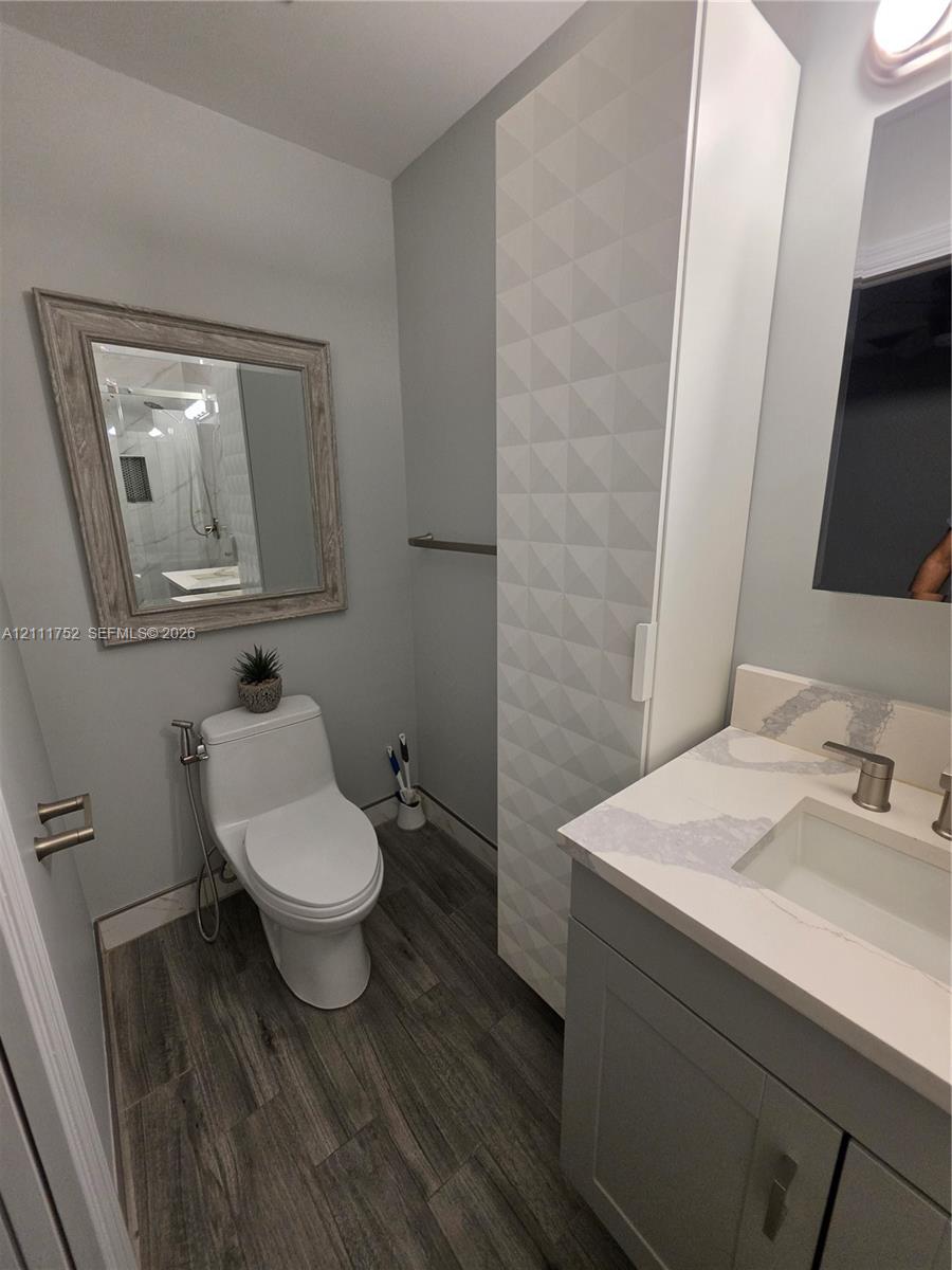 Bathroom featuring a vanity with a white composite countertop, integrated rectangular sink, tall geometric-patterned storage cabinet, and wood-finish flooring
