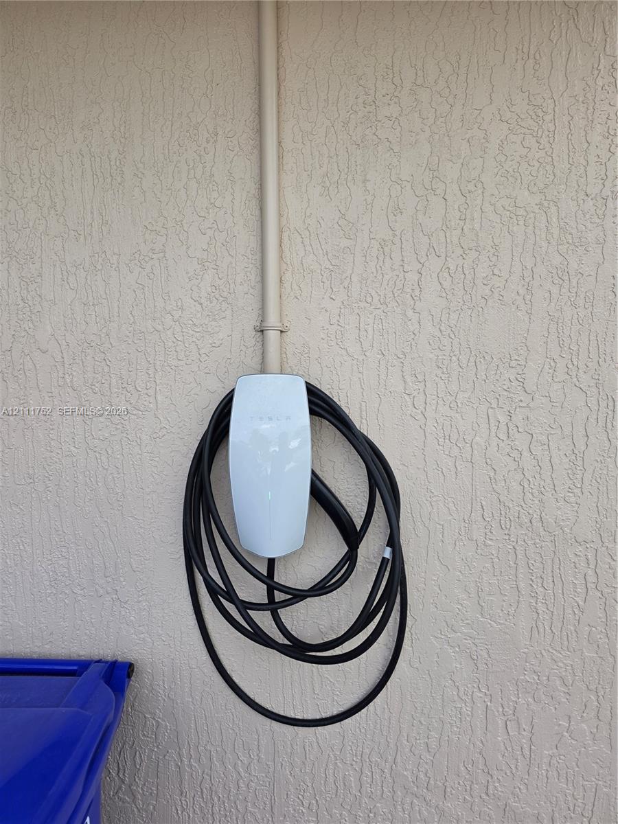 Wall-mounted electric vehicle charging station with exterior conduit and textured stucco wall finish