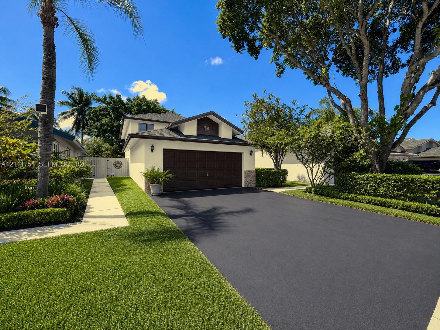 Exterior featuring a gabled roofline, concrete driveway, two-car garage with dark-finish door, stone-accented facade, and manicured landscaping