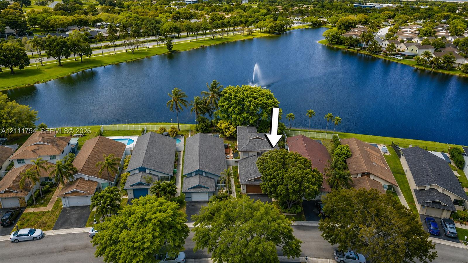 Aerial perspective of the waterfront property featuring a multi-gabled roofline, asphalt shingle roofing, paved driveway, and mature landscaping